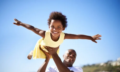 A father lifting his adorable daughter into the air while enjoying a day at the beach